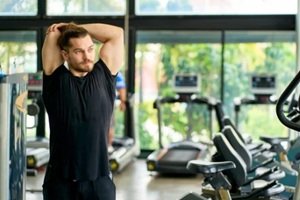 caucasian sport man in black sportswear stretching arms with cross-body shoulder stretch pose and warming up before weight training in fitness gym