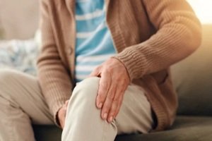 man on sofa and knee pain with injury for chronic illness, arthritis or fibromyalgia at home